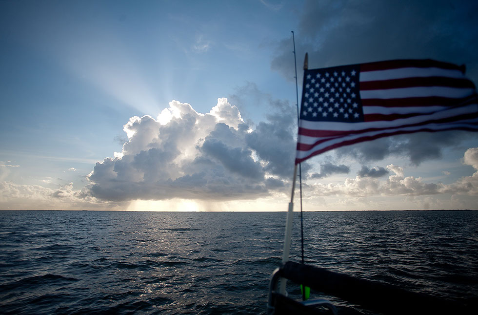 sun peeks from cloud over water behind our flag